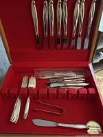 Full view of flatware set inside red felt–lined wooden chest showing knives, forks and tongs