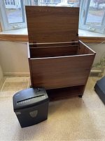 Rolling vertical file cabinet with hinged top lid open showing spacious interior and lower shelf, next to a black paper shredder.