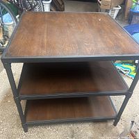 Front view of rustic side table showing wooden top and two wooden lower shelves with black metal frame.