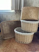 Four storage baskets of different sizes and weave patterns arranged on carpet near window.