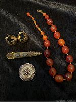 Full view of all five jewelry items on black fabric, showing necklace, earrings, brooches, and pin