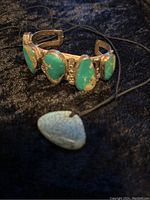 Silver-tone cuff bracelet and triangular turquoise pendant on black background