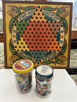 Vintage Chinese Checkers board with two jars of vintage marbles in front.