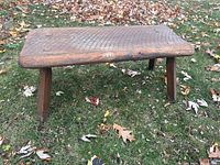 Full view of the primitive wooden bench showing the top surface and four sturdy legs on a grassy background.