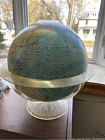 Spherical globe showing Northern Hemisphere with visible latitude and longitude lines, clear stand base on a wooden surface.