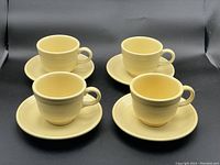 Four sunflower yellow ceramic cups on matching saucers, positioned on a black background for clear visibility of color and design.