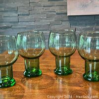 Four green glass goblets with rounded bowls and thick stems on wooden surface, arranged in a row