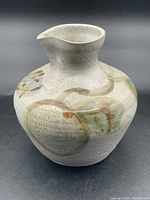 Full view of pottery pitcher showing shape and neutral textured glaze with decorative abstract patterns in muted earth tones