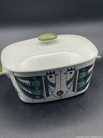 Side view of the covered baking dish showing stylized green and blue chicken motif with lid on.