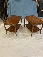 Pair of Deilcraft wooden side tables shown together, displaying their wooden finish, curved legs, and lower shelves.