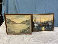 Two oil paintings side by side with wooden frames. Left is a landscape, right is boat scene at sunset.