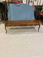 Photo of the full coffee table showing the wooden tabletop with scalloped trim and cabriole legs on a white sheet with blue backdrop.