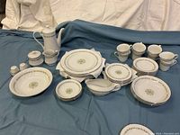 Full set displayed, including coffee pot with lid, cups, plates, bowls, salt and pepper shakers, cream pitcher, sugar bowl with lid, and gravy boat arranged on fabric background