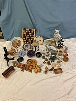 Photo showing a collection of ceramics, figurines, clock, glass vase, and small wooden decorative pieces arranged on a white cloth background.