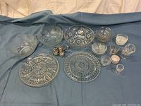 Full view of the glassware and condiment items spread on fabric background showing variety of platters, bowls, condiment set and small dishes.