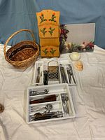 Overview of kitchen utensils arranged next to wicker basket, wooden letter box wall hanger, ceramic cup, seashells, and glass cutting board.