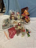 Full view of vintage Christmas decorations including plush reindeer, snowmen, tinsel garlands, stocking and ornaments spread on white surface