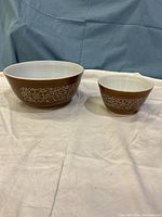 Two brown Pyrex mixing bowls side by side, showing front and side profile, with white floral pattern on brown exterior and white interior.