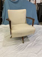 Front view of a mid-century modern pedestal swivel rocker chair with ivory fabric and wooden arms.