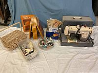 Full lot overview including sewing machine in case, Creative Hands books, sewing patterns, threads, buttons, and wicker basket with supplies.