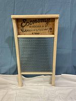 Front view of vintage washboard showing 'Economy Manufactured by Canadian Woodenware Co. St. Thomas' label on top wooden crossbar and glass washboard surface below.