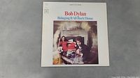 Front cover of Bob Dylan's 'Bringing It All Back Home' vinyl LP album showing two people seated in a living room with the title and artist's name printed at the top.