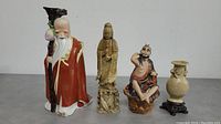 Full view of all four items including two ceramic male figurines, one soapstone female figurine, and soapstone vase with stand