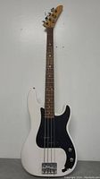 Full front view of white electric bass guitar with black pickguard and natural wood neck and headstock, showing overall shape and condition.