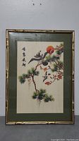 Framed Chinese silk embroidery artwork showing birds on pine branches with calligraphy and a red sun.