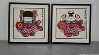 Pair of framed Japanese watercolor artworks depicting girls holding large pink fish, side by side