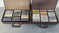 Two open briefcase-style boxes filled with cassette tapes arranged in rows showing various artist names on spines