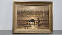 Framed vintage painting showing a rural farming scene with a man and buffalo in plowed field, homes in background.