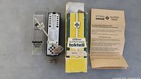 Top view of Wittner metronome, original box, plastic case, winding key, and instructions set on gray surface.