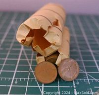 Two original paper rolls with ends partially open, showing Canadian pennies inside, one loose penny in front. Coins are copper with circulated patina.