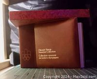 Photo of the brown binder album for the Olympic Stamp Souvenir Collection with gold embossed text and Olympic rings logo, showing the cover and spine.