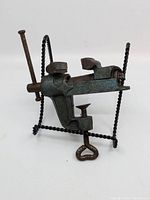 Photo of antique 2-inch cast iron portable bench vise showing clamp and screw mounting mechanism from an angled front-side view.