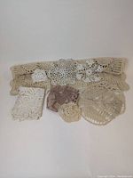 Nine crochet doilies including one large beige long rectangular table runner and various smaller white, cream, beige, and brown lace-patterned doilies in different shapes and sizes.