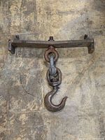 Full view of the Crosby Laughlin industrial swivel hook mounted on a rectangular cast iron plate with two hooks on each end. Shows the hook hanging vertically on a textured surface.