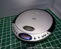 Photo of the top and angled front view of the portable CD player showing its silver round design, buttons across the front edge, and an oval display.