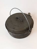 View showing entire cast iron Dutch oven with lid and bail handle, illustrating overall shape and condition.