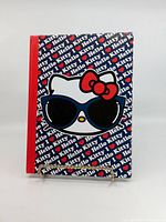 Front cover of Hello Kitty notebook with red spine and large Hello Kitty face wearing sunglasses on a blue repeating background pattern saying 'Hello Kitty' and red bows.