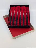 Six Japanese steak knives in a black and beige box with red velvet interior lining, arranged in individual slots.