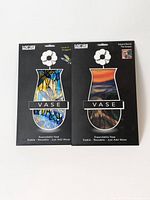 Front view of two unopened Modgy expandable flower vases in packaging, showing art designs and white flower clips on top. One vase shows The Scream by Edvard Munch, the other the Dragonfly design by Louis C. Tiffany.