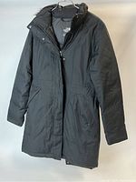 Front view of the black North Face women's down jacket hanging, showing the closed front with zipper and snap buttons, two front pockets and long sleeves.