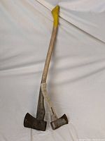 Photo showing two axes crossing each other, one with yellow paint on handle top.