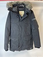 Front view of black TNA duck down insulated winter jacket with fur trim on hood and multiple pockets.
