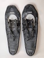 Top view of the pair of Tubbs Wilderness model 30 inch snowshoes showing the black camo design, metal frames, bindings, and heavy vinyl webbing.
