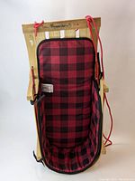 Front view of the wooden sled with attached red and black plaid cushioned sleigh pad, showing overall condition and structure.