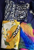 Four silk scarves displayed. Two matching blue and white floral scarves, yellow floral and fruit patterned scarf, and one multicolored tie-dye scarf with pink border.