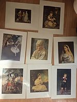 Nine assorted art prints laid out on a wooden floor, showing various historical and classical portraits and scenes, each approximately 10 x 12 inches in size.